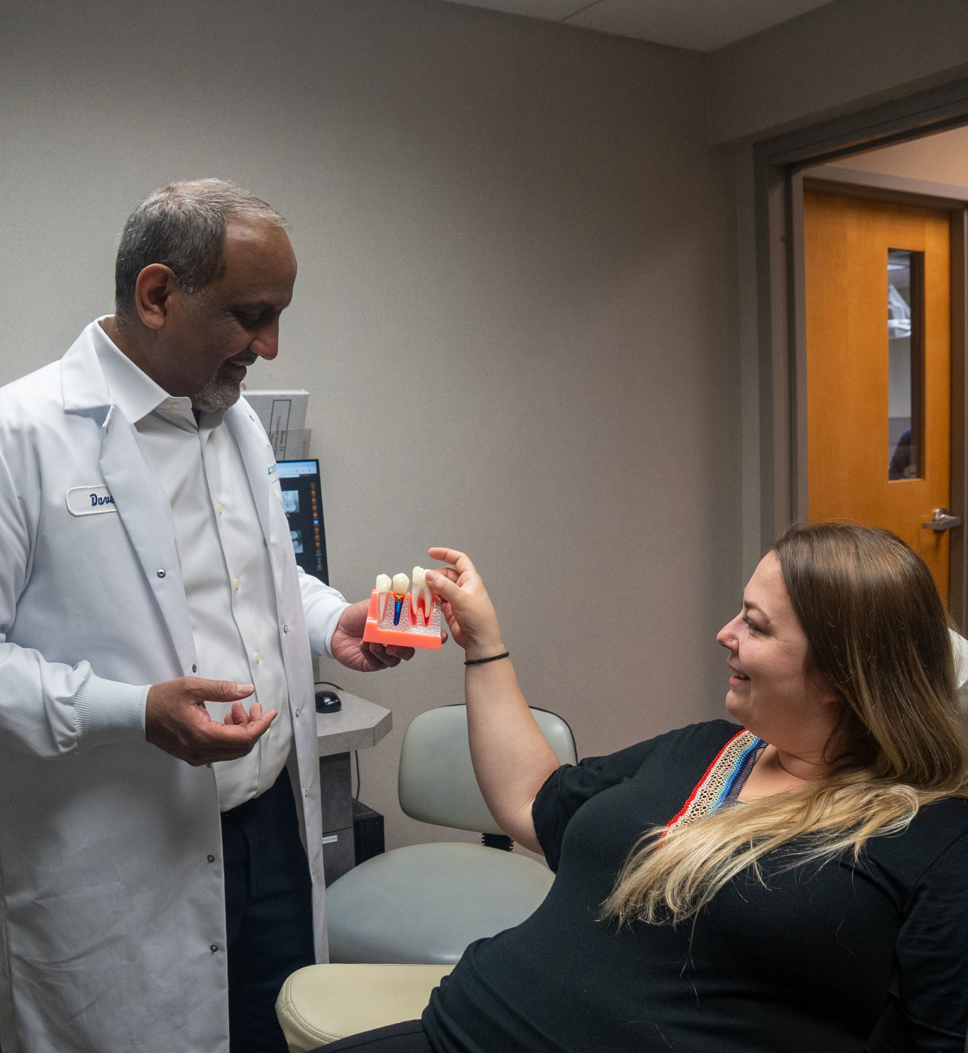 Dr. Rahman showing tooth extraction model to patient in exam room